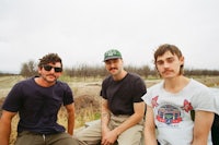 three men sitting on top of a truck in a field