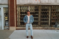 a man in jeans and a denim jacket standing in front of a building