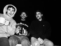 three men sitting on a bench with a cup of coffee